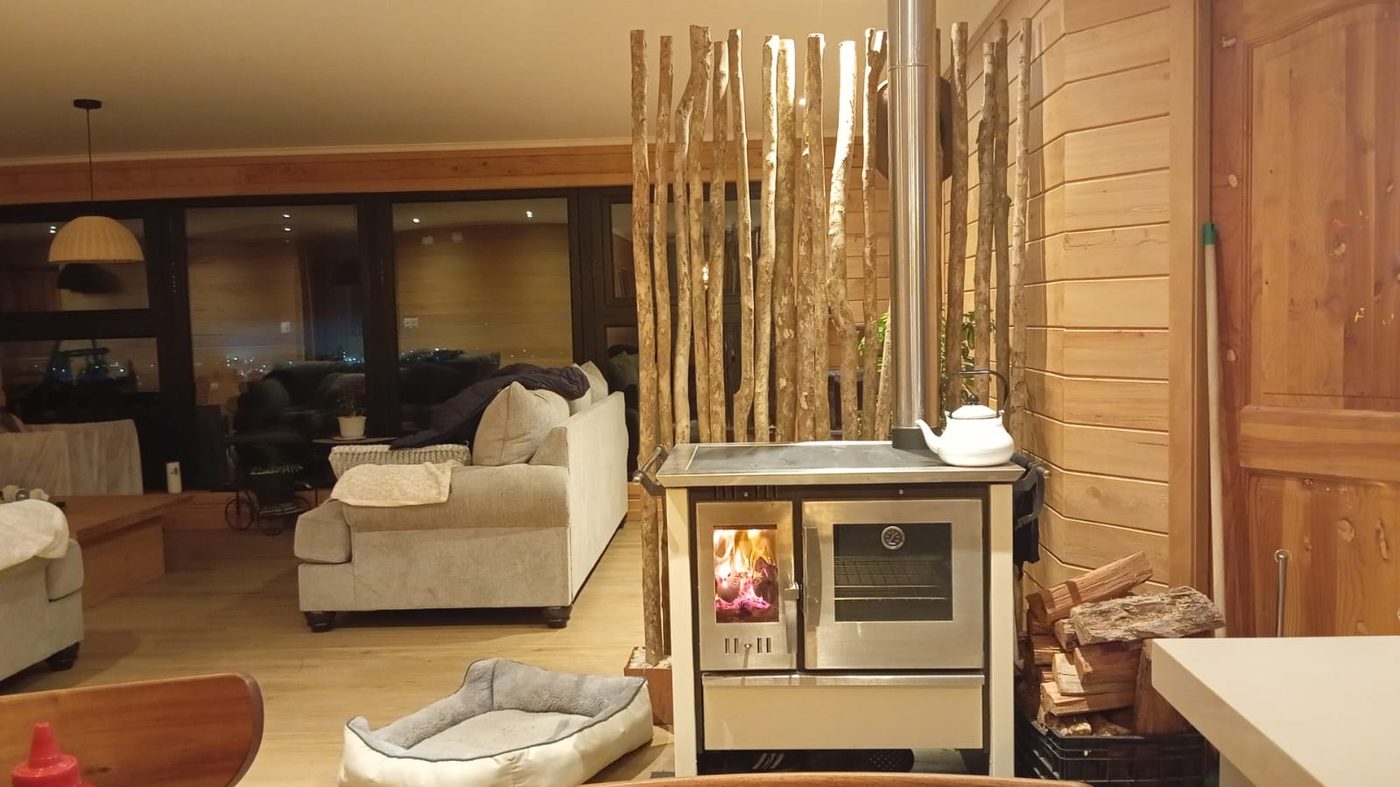 Living con cocina a leña y revestimiento de madera en una casa construida por Rahue en Chiloé